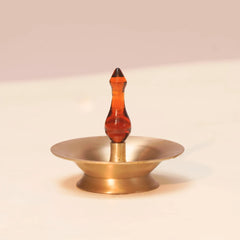 Baby Vilakku Oil Lamp, brass saucer with amber borosilicate glass finial, front view on plain background