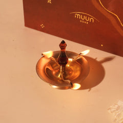 Baby Vilakku Oil Lamp lit at three wicks, brass saucer and amber glass finial, gift box behind, top angle