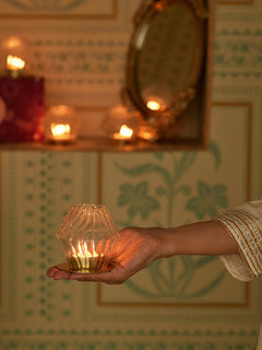 Hand holding a lit candle holder in diamond shape on gold plated metal plate with a decorative background
