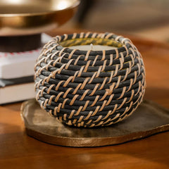 A round woven candle holder, sitting on a rustic bronze-colored aluminium tray.