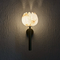 Wall-mounted Lotus Alabaster Wall Sconce with a glowing, petal-shaped translucent shade and a dark metal stem, mounted on a textured dark gray wall.