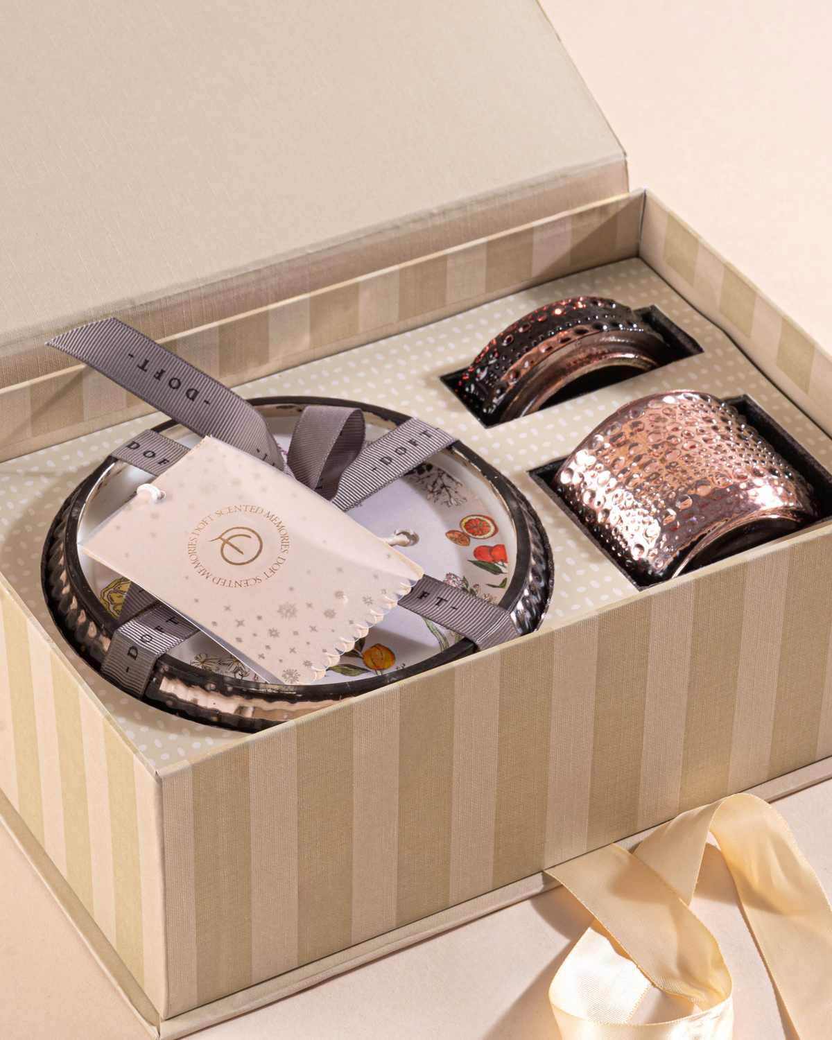 A gift box containing a set of scented designer premium candles, with a branded paper tag and ribbon.