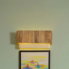 Unique Tokyo Wooden wall sconce casting a warm glow on a light green wall with a framed artwork below. 