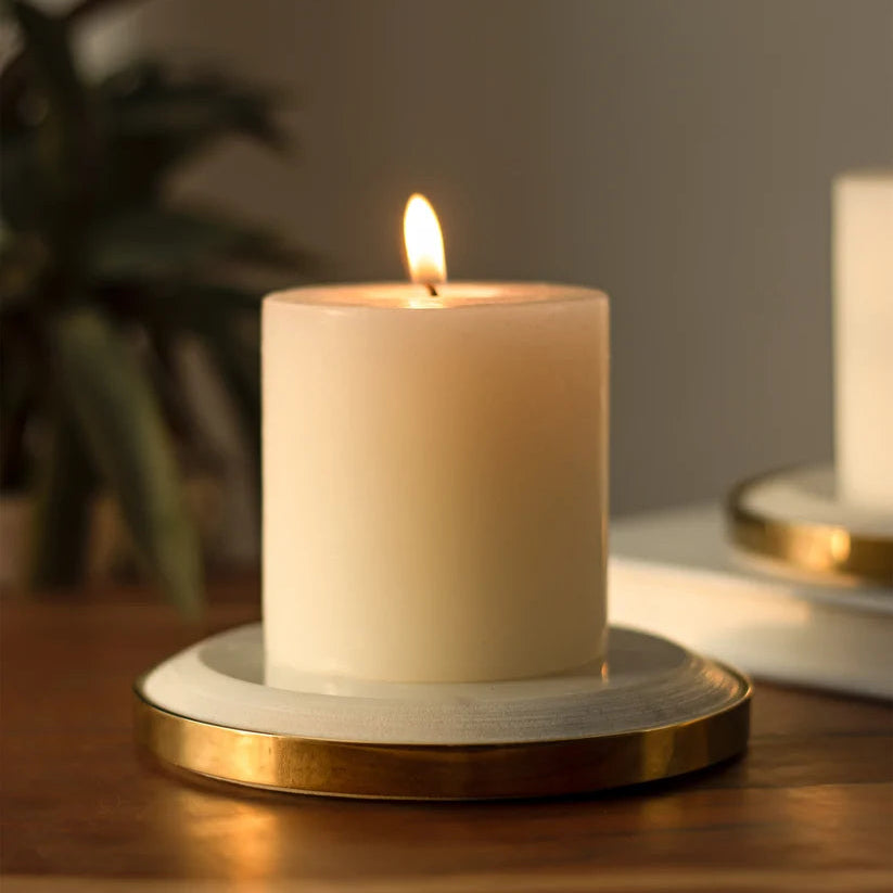 Round white and gold Yang Candle Plate with a lit cream-colored pillar candle, set on a wooden table with a softly blurred background.