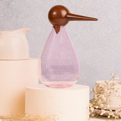 A whimsical bird-shaped hand-blown glass jar with a pink body and a brown beak, displayed on a neutral background.