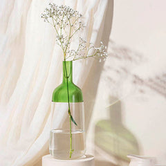 A green and clear glass iris vase with a tall neck and flared base, displaying a single flower stem, placed on a white surface with a light background.