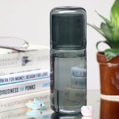 Clear Juliette Glass Carafe in grey color with cap on a surface with books and a plant in the background