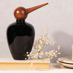A black glass jar with a bird-shaped top, placed on a table with a few white flowers beside it.