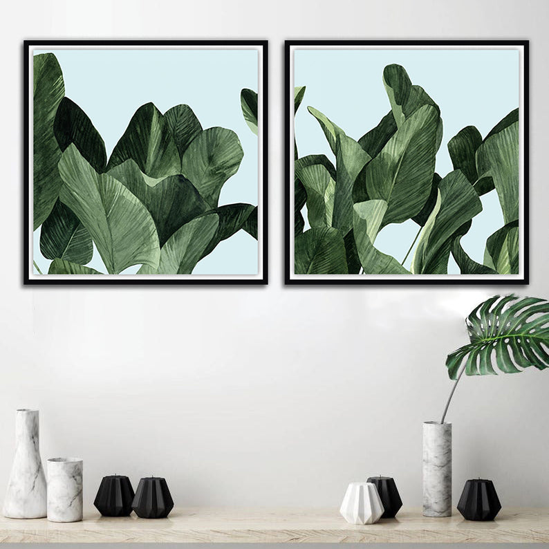 Two framed art prints featuring a green palm leaf pattern on a blue background, displayed on a wall above a marble surface with decorative objects.