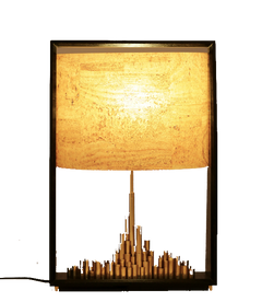 Table lamp with a brass cityscape base and a warm glowing cork sheet shade with wood finish stand.