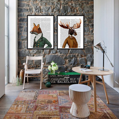Two framed art prints hanging on a stone wall. The left frame depicts a fox in a green military uniform, and the right frame shows a moose in a brown coat with antlers.