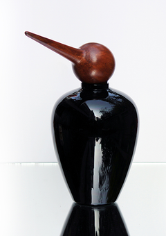 Decorative glass jar in black with a bird-shaped top, placed on a reflective surface