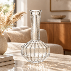A clear ribbed glass decanter with a flared base sits on a marble table in a softly lit living room.