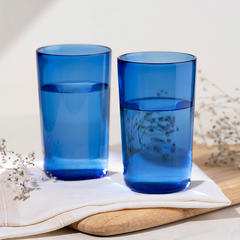 Two blue glass lowball Juliette Glasses on a white cloth, with a sprig of dill leaves decoration.