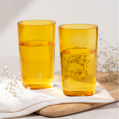 Two yellow borosilicate glass highball glasses placed on a white surface with a white napkin beside them.