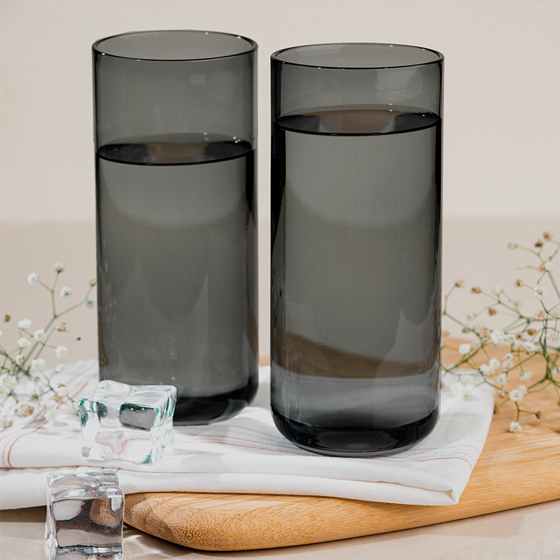 Two grey colored cocktail glasses filled with a clear liquid, placed on a white surface with ice cubes and decorative flowers in the foreground.
