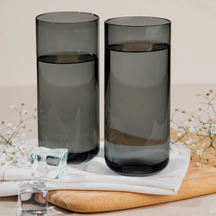 Two grey colored cocktail glasses filled with a clear liquid, placed on a white surface with ice cubes and decorative flowers in the foreground.