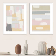 Two framed abstract pastel color artworks hanging on a wall above a shelf with decorative items.