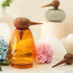 Decorative glass Chirp Penguin bird design with wooden beak and head on a light surface with flowers.