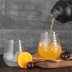Premium 2 clear ribbed stemless glasses with a twisted design, with juice pouring from a bottle in one of the glass. 